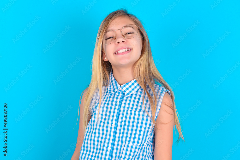 little kid girl with glasses wearing plaid shirt over blue background with broad smile, shows white teeth, feeling confident rejoices having day off. little kid girl with glasses wearing plaid shirt over blue background with broad smile, shows white teeth, feeling confident rejoices having day off.
