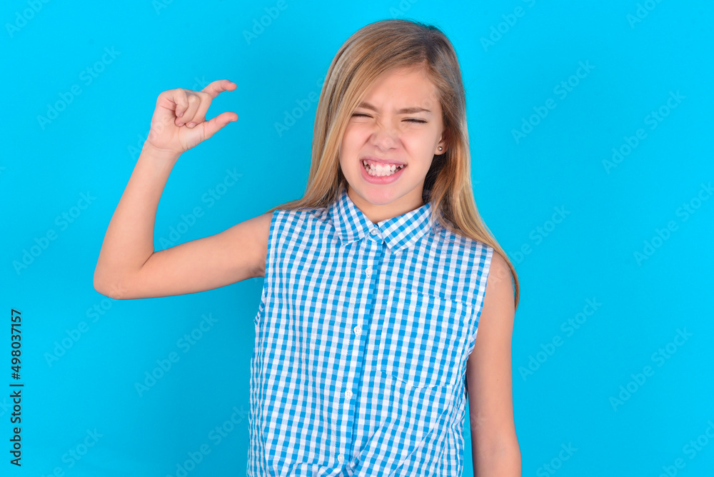 little kid girl with glasses wearing plaid shirt over blue background  smiling and gesturing with hand small size, measure symbol.