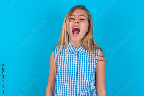 Canvas Print Stressful little kid girl with glasses wearing plaid shirt over blue background  screams in panic, closes eyes in terror, keeps hands on head, finds out terrified news, can't believe it