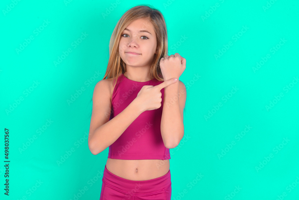 blonde little kid girl wearing pink sport clothes over green background in hurry pointing to watch time, impatience, upset and angry for deadline delay blonde little kid girl wearing pink sport clothes over green background in hurry pointing to watch time, impatience, upset and angry for deadline delay