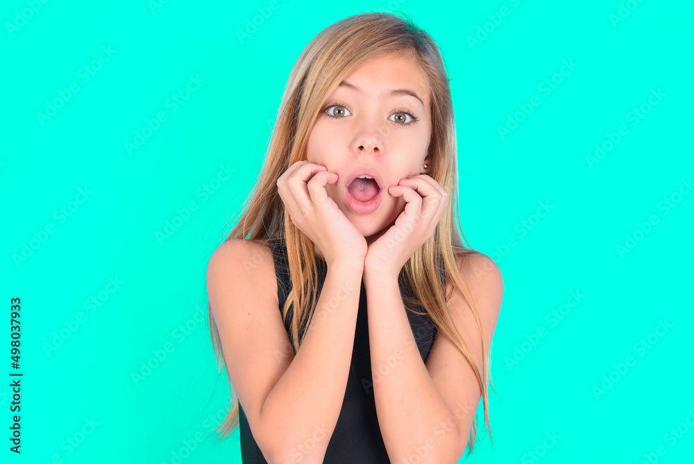 Speechless blonde little kid girl wearing black sport clothes over green background keeps hands near opened mouth reacts to shocking news stares wondered at camera Speechless blonde little kid girl wearing black sport clothes over green background keeps hands near opened mouth reacts to shocking news stares wondered at camera