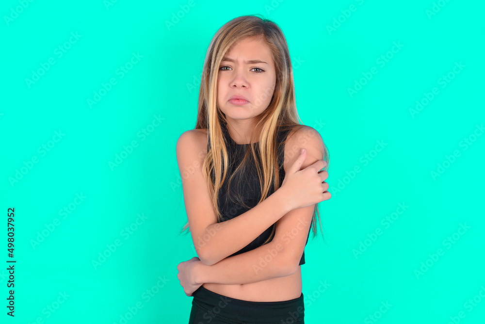 blonde little kid girl wearing black sport clothes over green background shaking and freezing for winter cold with sad and shock expression on face. blonde little kid girl wearing black sport clothes over green background shaking and freezing for winter cold with sad and shock expression on face.