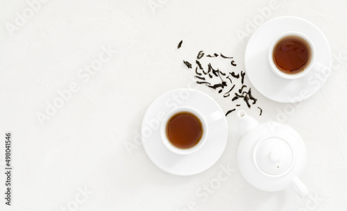two white cups of black tea, next to a white teapot for brewing a drink, white non-uniform background, flat lay, flat lay, flat lay, top view, copy space, mockup