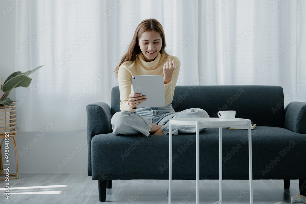 A woman plays a tablet on the sofa in her living room at home, she is resting on weekends after a hard day's work, she relaxes by watching movies and listening to music on her tablet. Holiday concept.
