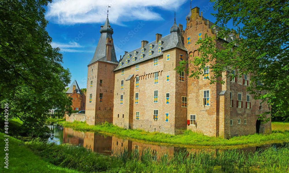 View beyond green park with moat on medieval dutch water castle from 14th century against blue summer sky - Kasteel Doorwerth near Arnhem, Netherlands
