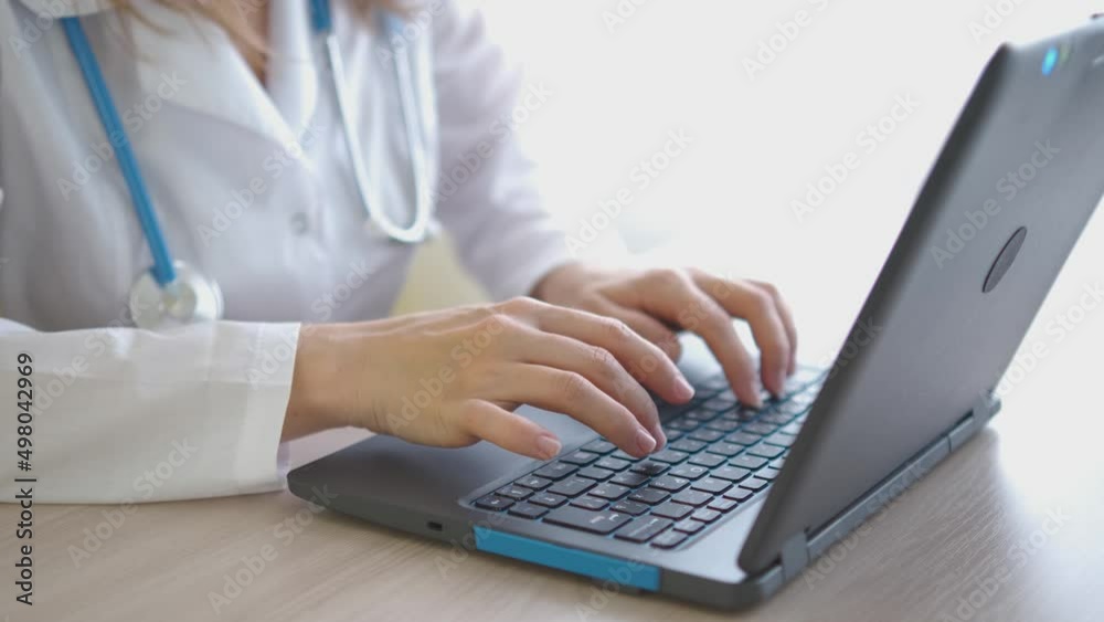 A girl in a white coat works on a laptop on the table close-up. Female hands on the keyboard. Doctor's office A girl in a white coat works on a laptop on the table close-up. Female hands on the keyboard. Doctor's office