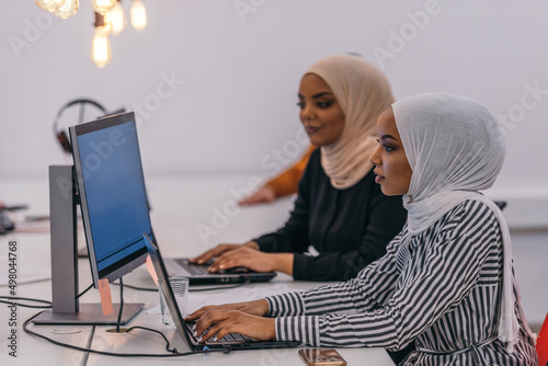 Close-up portrait of a beautiful, charming, young woman with a hijab looking at her computer and sitting next to her colleague in an office..