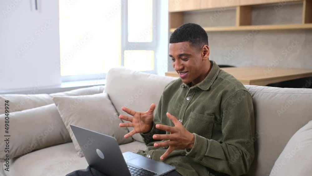 Cheerful carefree guy using laptop computer for video connection, looking at the webcam and waving hand. Man sitting at the sofa and making video call to somebody Cheerful carefree guy using laptop computer for video connection, looking at the webcam and waving hand. Man sitting at the sofa and making video call to somebody