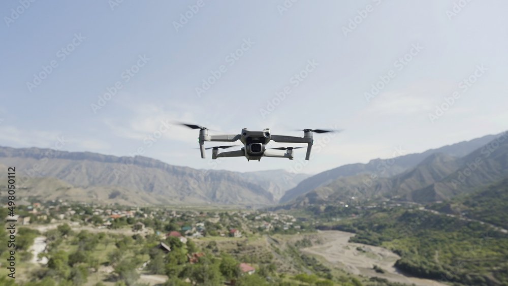 Quadcopter hanging in the air above green valley and growing trees