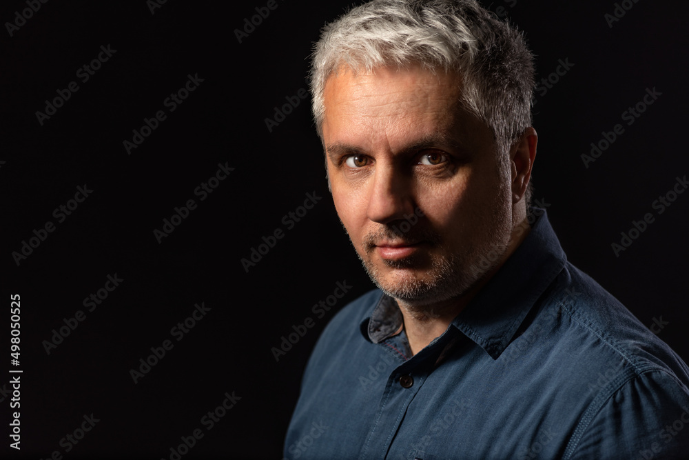 Head and shoulders low key portrait of a bearded middle-aged man looking thoughtfully at the camera over a black studio background with copy space