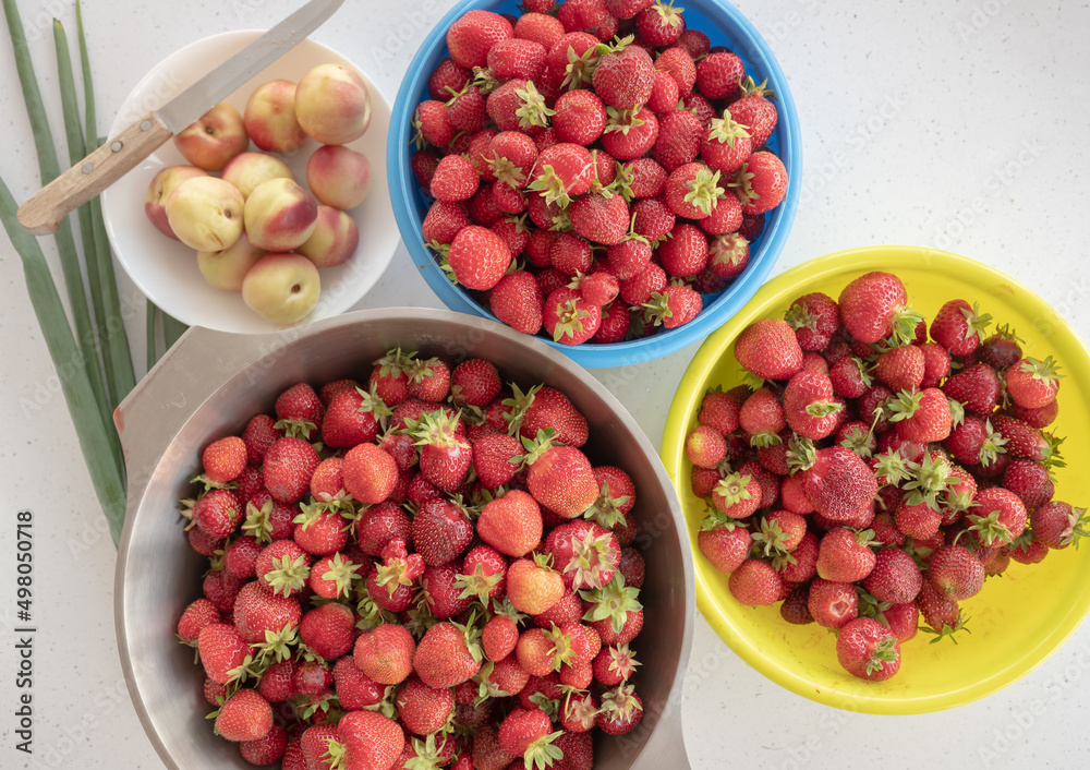 top view of fresh strawberries in bowls next to a bowl of peaches and green onions. top view of fresh strawberries in bowls next to a bowl of peaches and green onions.