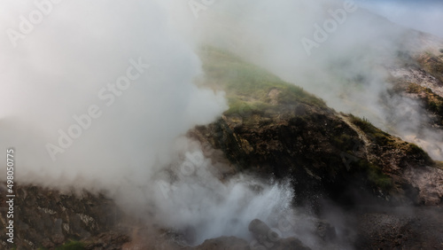 Water boils in the cauldron of the geyser. Spray and hot steam rise over the hillside. Everything is shrouded in haze. Poor visibility. Kamchatka. Valley of Geysers