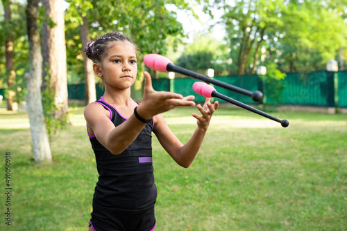 Girl doing exercise with clubs on rhythmic gymnastics training outdoors in summer in sports camp