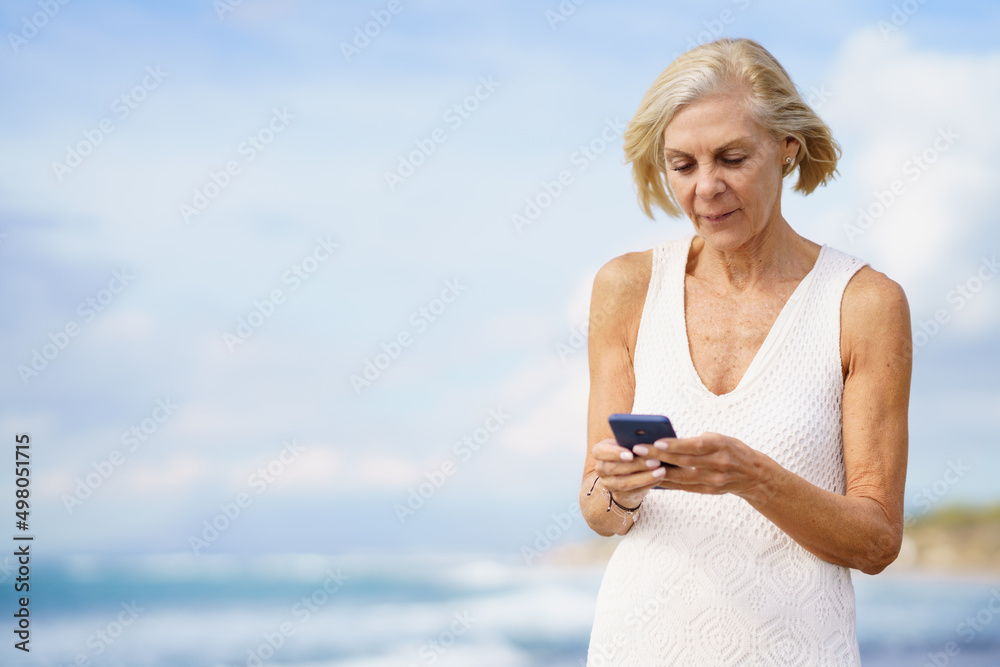 Mature woman walking on the beach using a smartphone. Mature woman walking on the beach using a smartphone.