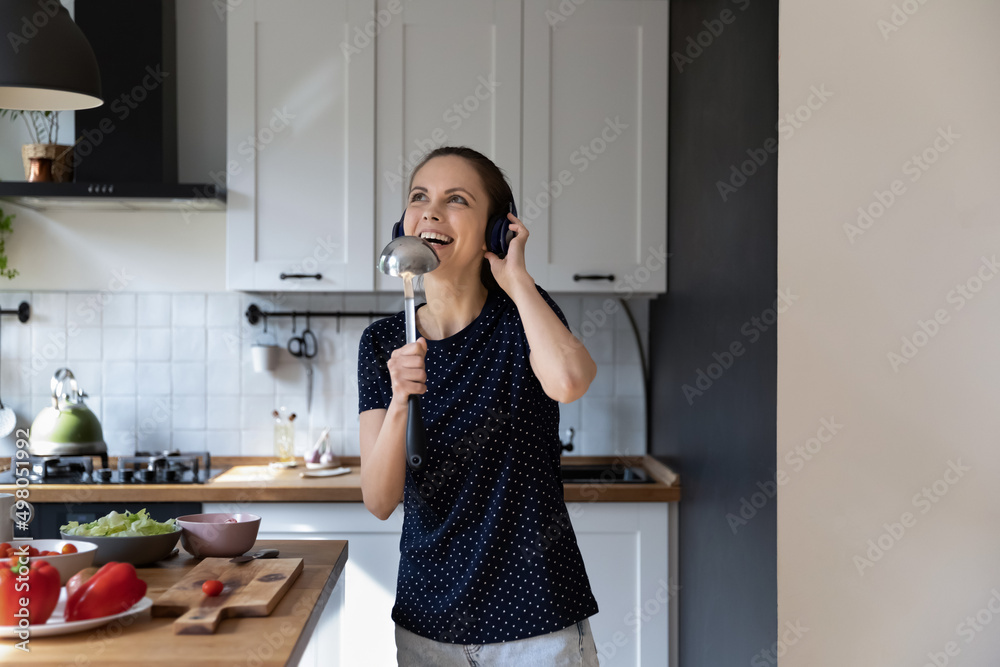 Woman sing song use ladle like mike, distracted from cookery in kitchen, listen music through headphones, dancing, enjoy weekend feels carefree while cooks vegan food. Hobby, karaoke at home concept Woman sing song use ladle like mike, distracted from cookery in kitchen, listen music through headphones, dancing, enjoy weekend feels carefree while cooks vegan food. Hobby, karaoke at home concept
