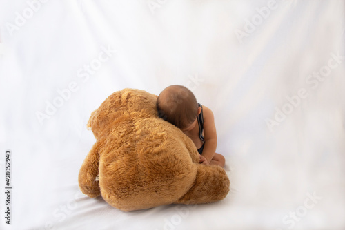 Portrait of baby wrapped in teddy bear. The shy baby hides his face. Empty text space on white background