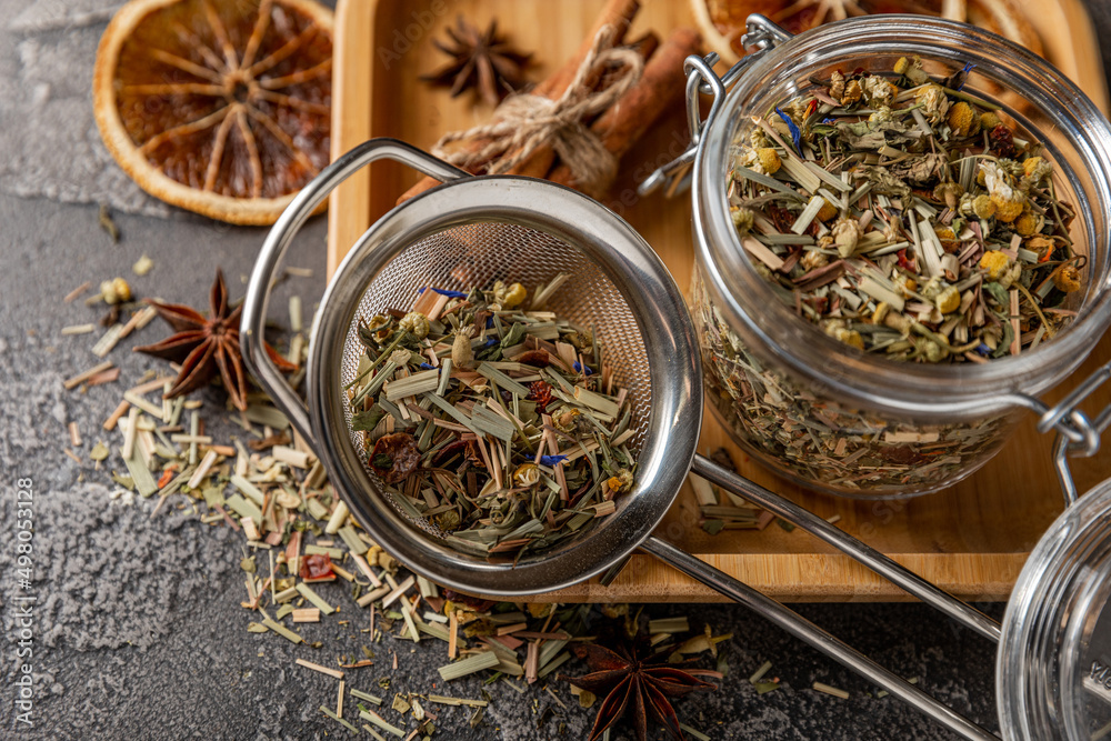 Fototapeta premium Herbal tea in a brewing strainer on a black textured background. Detox and tea for immunity. Herbal collection of chamomile, mint, lemon balm. pieces of wild rose and dried fruits.