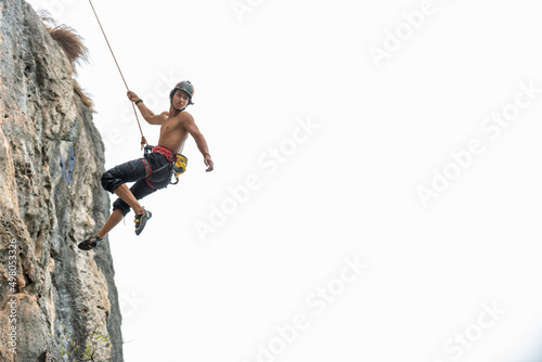 Confidence young Asian man climber with safety rope climbing on rocky mountain at tropical island in sunny day. Strong handsome male enjoy outdoor active lifestyle and extreme sport on summer vacation © CandyRetriever 