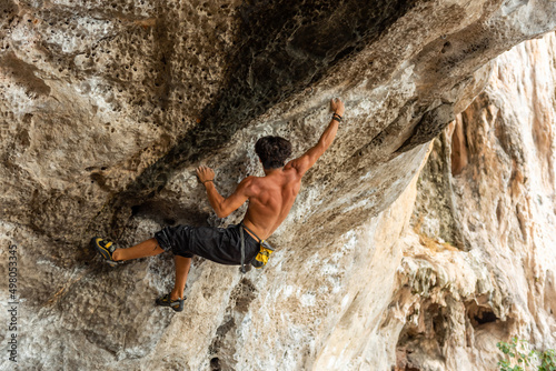 Confidence young Asian man climber climbing on rocky mountain at tropical island in sunny day. Strong handsome male enjoy outdoor active lifestyle and extreme sport climbing on summer vacation