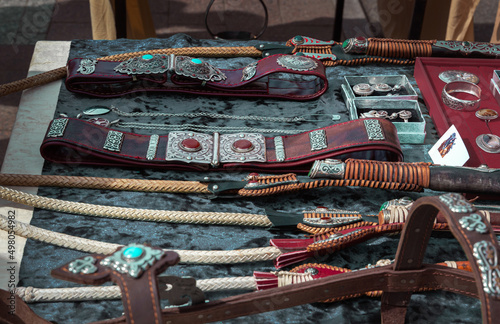 Leather belts inlaid with silver and stones, riders' whips, handmade horse harness in traditional Asian style lie on the counter of a street stall photo