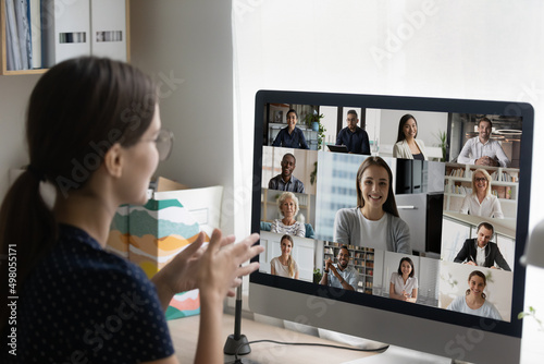 Businesswoman sit at workplace desk with computer, speak to colleagues, business team or clients use video conference application, diverse people on monitor screen view. Group video call event concept
