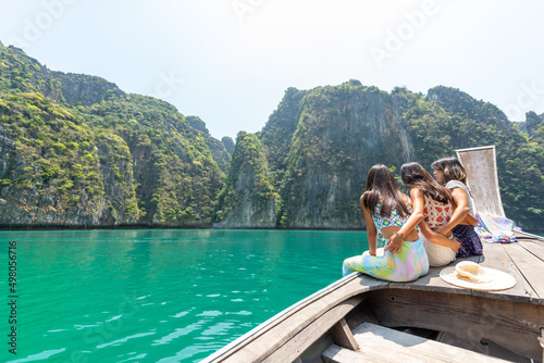 Group of Young beautiful Asian woman sitting on the boat passing island beach lagoon in summer sunny day. Happy female friends enjoy and fun outdoor lifestyle together on summer vacation in Thailand