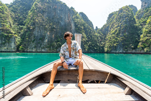 Portrait of Young handsome Asian man sitting on the boat passing beach lagoon in summer sunny day. Healthy guy relax and enjoy outdoor lifestyle on travel vacation at tropical island in Thailand
