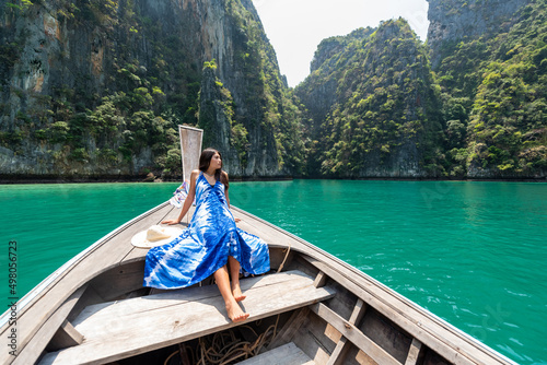 Young beautiful Asian woman in blue dress sitting on the boat passing island beach lagoon in summer sunny day. Happy female relax and enjoy outdoor lifestyle together on summer vacation in Thailand © CandyRetriever 