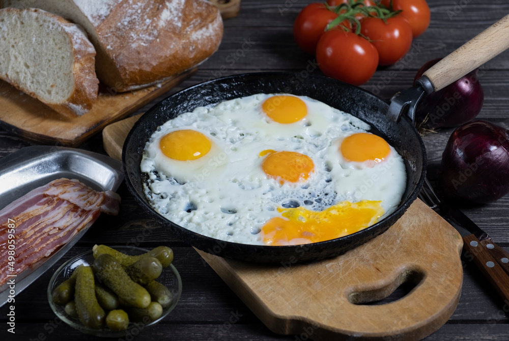 rustic fried eggs on a dark wooden table with tomatoes, a glass of vodka, beacon, bread and pickled gherkins. in a dark key