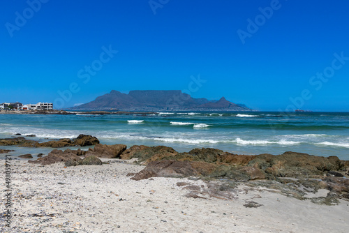 Fototapeta Naklejka Na Ścianę i Meble -  Beach, rocks and ocean with Table Mountain in the background. Against a clear blue sky. 