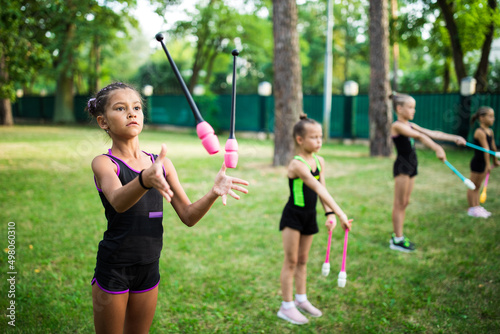 Girl doing exercise with clubs on rhythmic gymnastics training with other trainees outdoors in summer in sports camp © Olena Shvets