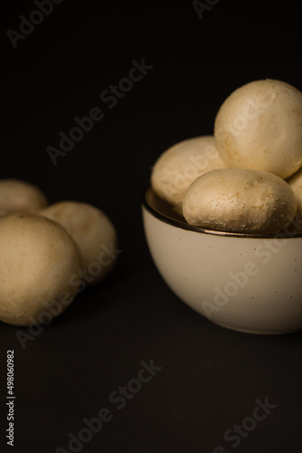 Champignon mushrooms in a plate on a dark background, ready for cooking.