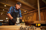 Senior Professional carpenter in uniform working of manual milling machine in the carpentry workshop