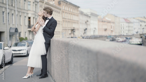 Beautiful couple of newlyweds embracing on background of city. Action. Photo shoot for newlyweds in urban environment. Beautiful newlyweds embrace in city with old architecture