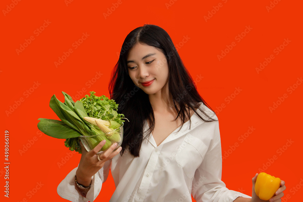Vegetarian concept, Healthy woman hold bell pepper and bowl of fresh vegetable on orange background Vegetarian concept, Healthy woman hold bell pepper and bowl of fresh vegetable on orange background