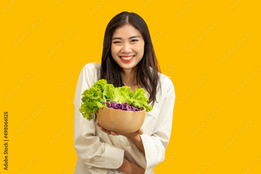 Vegetarian concept, Healthy woman holding bowl of mix vegetable salad on isolated yellow background Vegetarian concept, Healthy woman holding bowl of mix vegetable salad on isolated yellow background