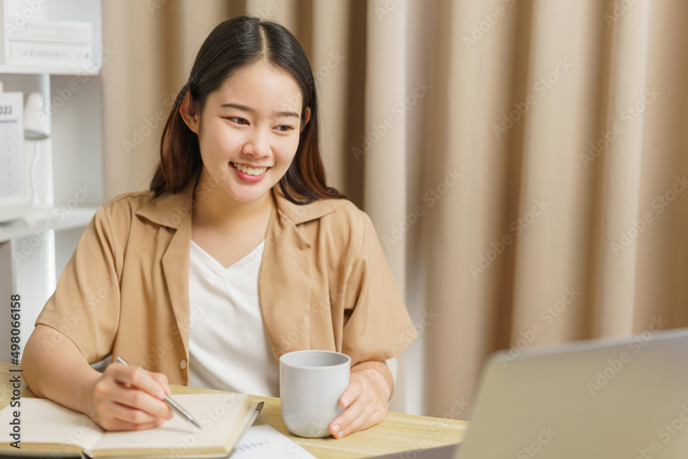 Online lifestyle concept The female home worker writing down the information presenting on the notebook with a coffee mug. Online lifestyle concept The female home worker writing down the information presenting on the notebook with a coffee mug.