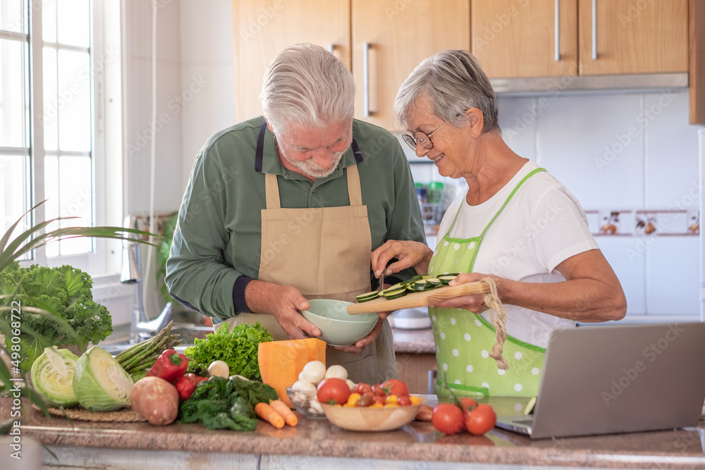 Attractive senior couple working together in home kitchen preparing vegetables and zucchini. Elderly smiling couple enjoying healthy lifestyle
