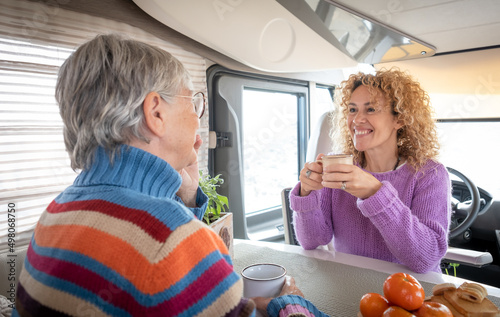 Two caucasian women mother and daughter or friends sitting inside a camper van motor home talking drinking a coffee cup. Lifestyle and travel modern people, vacation journey concept photo