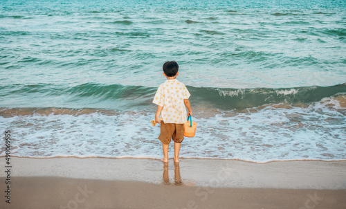Back view of little boy standing on the beach looking at the sea, beautiful sky in evening.Children's Obstacles Theme.