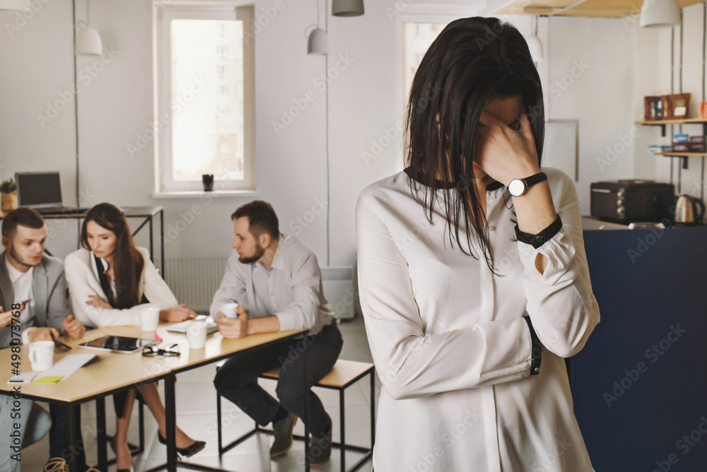 Woman crying in the office and covered her face with her hands and her colleagues are laughing on the background. Bullying and stress at the workplace Woman crying in the office and covered her face with her hands and her colleagues are laughing on the background. Bullying and stress at the workplace