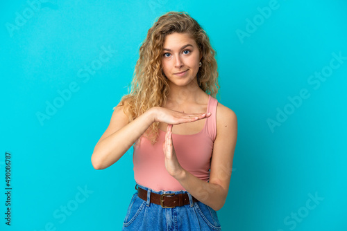Young blonde woman isolated on blue background making time out gesture © luismolinero