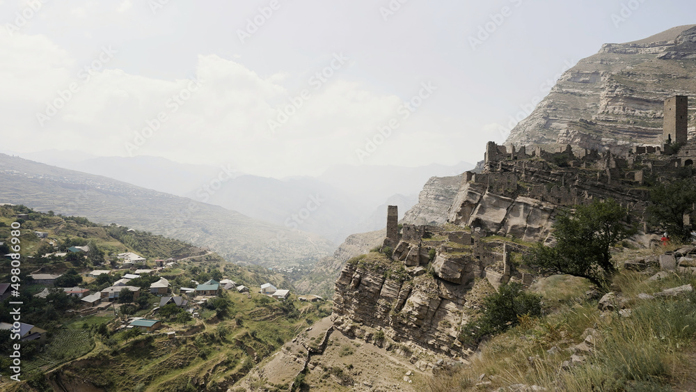 Ruins of ancient village with abandoned building stone walls on a mountain slope. Action. Summer cliff and residential settlement near the rock on cloudy sky background.