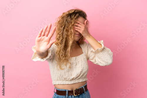 Young blonde woman isolated on pink background making stop gesture and covering face
