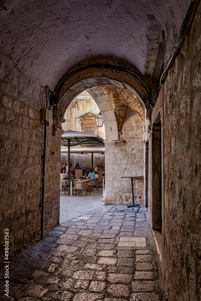 Narrow pavement alley through an archway in the old town of Dubrovnik with a cafe in the backgrownd