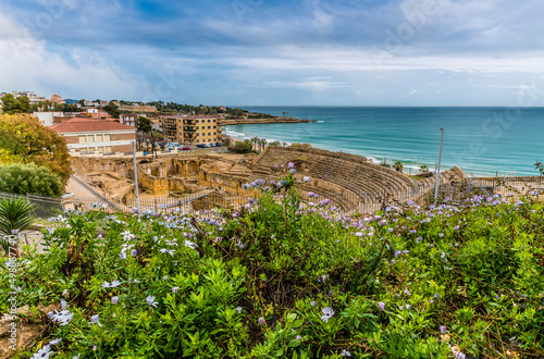 A view past bushes towards the ancient Roman amphitheatre ruins in the city of Tarragona on a spring day