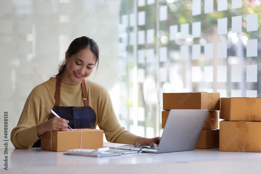 Shipping shopping online, startup small business owner writing address on cardboard box at workplace. Freelance Asian woman small business entrepreneur SME working with box at home. Shipping shopping online, startup small business owner writing address on cardboard box at workplace. Freelance Asian woman small business entrepreneur SME working with box at home.