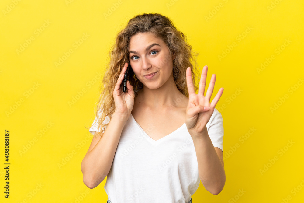 Young blonde woman using mobile phone isolated on yellow background happy and counting four with fingers Young blonde woman using mobile phone isolated on yellow background happy and counting four with fingers