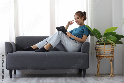 Cheerful Asian young woman lifestyle while sitting on sofa at home using tablet and having fun.