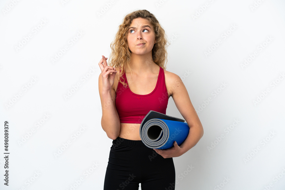 Young sport blonde woman going to yoga classes while holding a mat isolated on white background with fingers crossing and wishing the best Young sport blonde woman going to yoga classes while holding a mat isolated on white background with fingers crossing and wishing the best